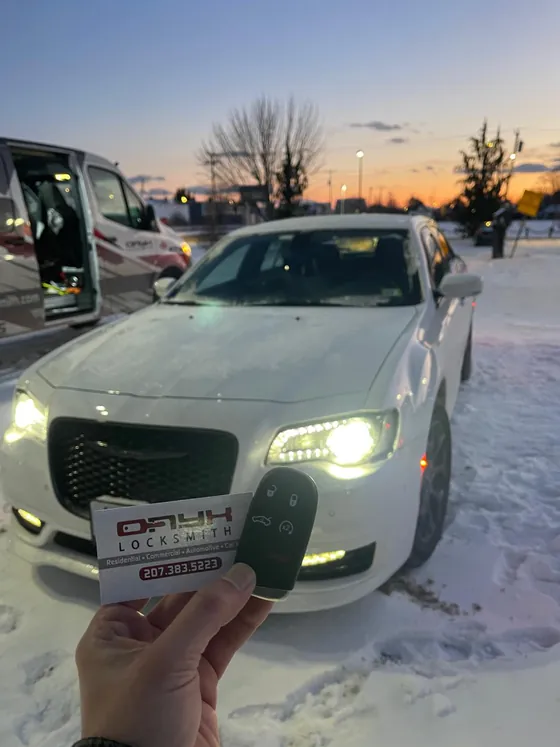 A new key fob and an Onyx card held up at a white Chrysler 300 at dusk